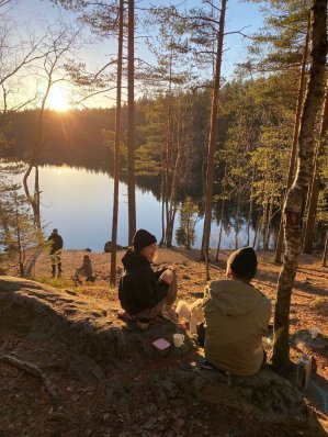 Kaksi ihmistä istuu kalliolla kahvilla syksyisessä auringonpaisteessa